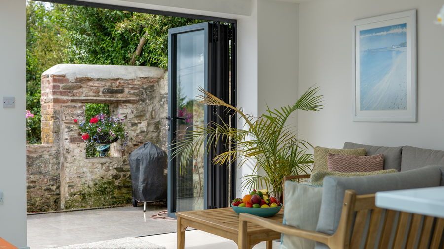 Sunroom with open folding doors, looking onto a brick wall patio with a grill and garden greenery.