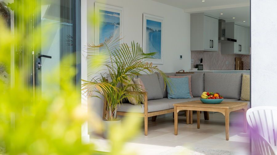 Outdoor patio with couch and small table, view of kitchen, fruit bowl, palm plant, artwork, bright.