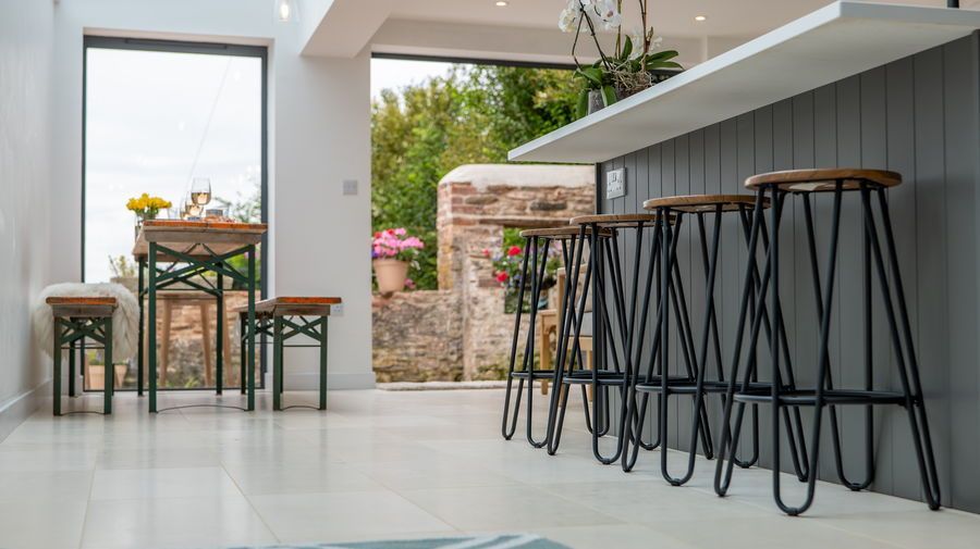 Modern kitchen with a breakfast bar, high stools, and a small table overlooking a garden view.