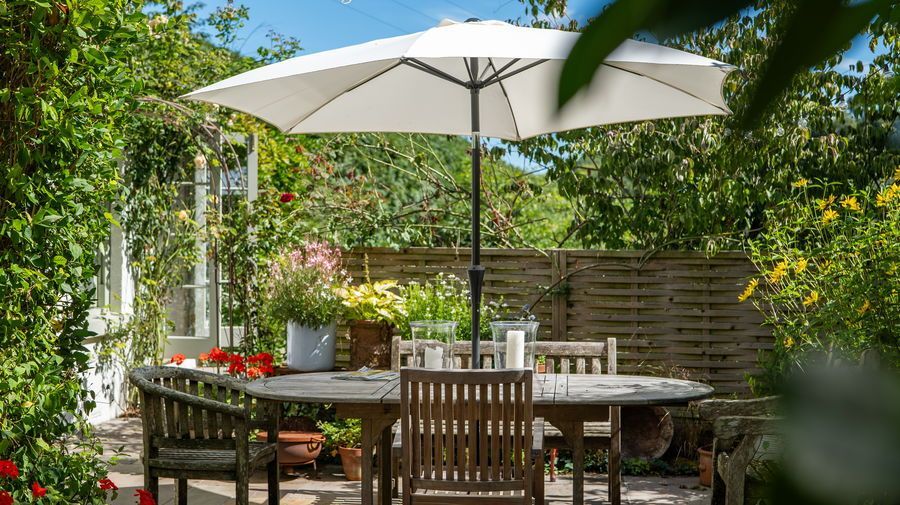 Patio with wooden furniture, umbrella, and lush greenery.