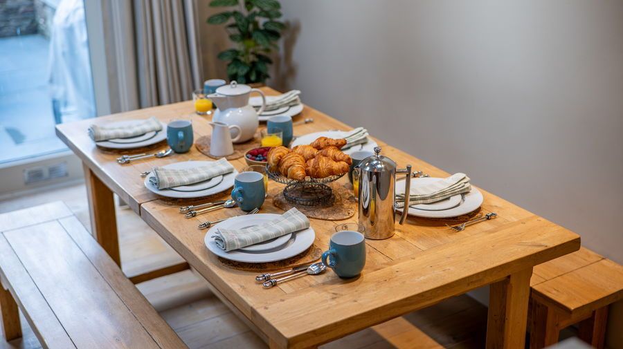 Wooden dining table set for breakfast with plates, pastries, and drinks.