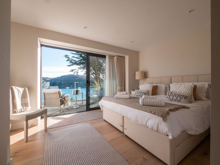 Bedroom with a large window overlooking a body of water. Beige decor, bed, rug, and balcony.