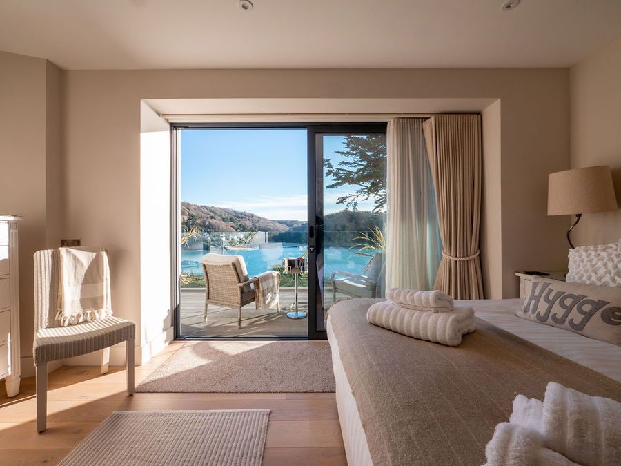Bedroom with large sliding doors overlooking a scenic bay. Includes bed, chair, and neutral decor.