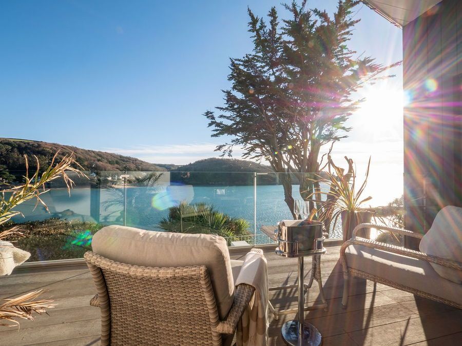 Patio with chairs overlooking a blue body of water, trees, and bright sunshine.