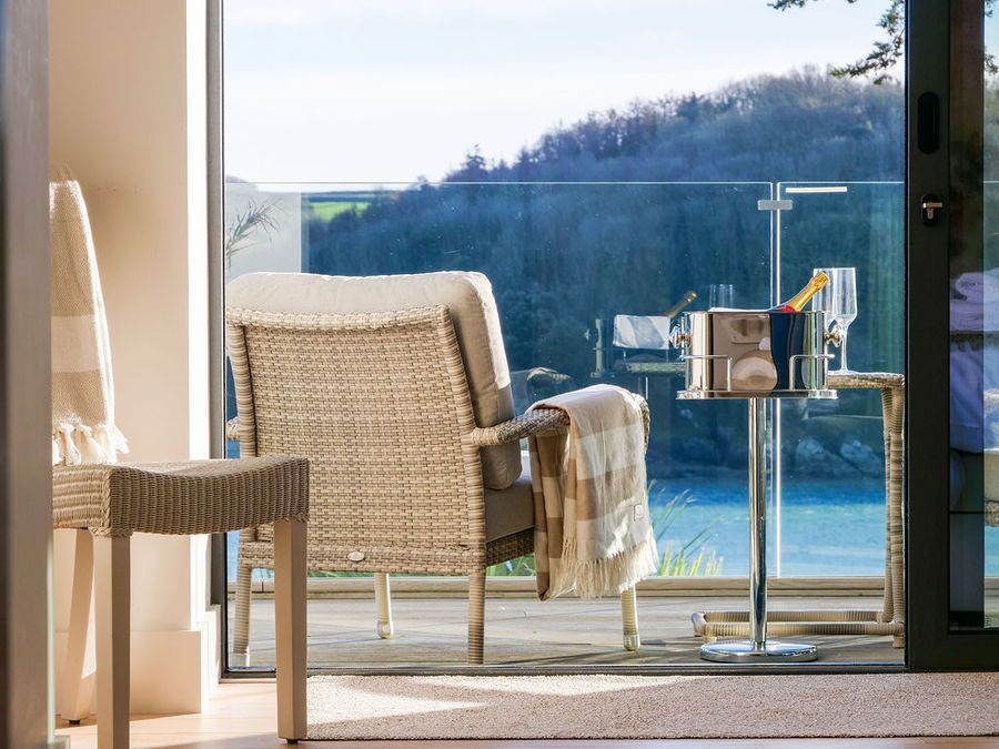 Patio seating with a view: woven chair, blanket, side table, glass railing overlooking water and trees.