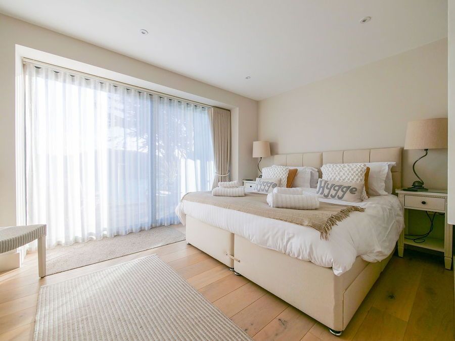 Bright bedroom with a large bed, light curtains, and a wooden floor.