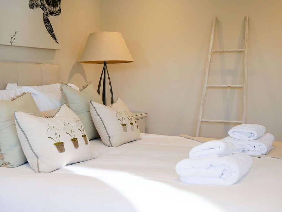 Bedroom with made bed, pillows, lamp, and folded towels. A ladder leans against the wall.