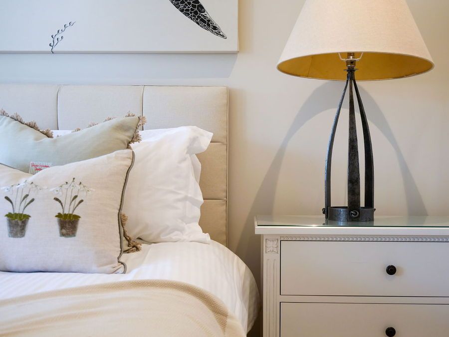 Bedroom interior with white headboard, bedside table, lamp, and decorative pillows.