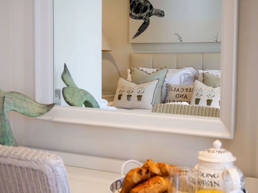 Mirror reflecting a bed with pillows and artwork, breakfast croissants and tea in foreground.