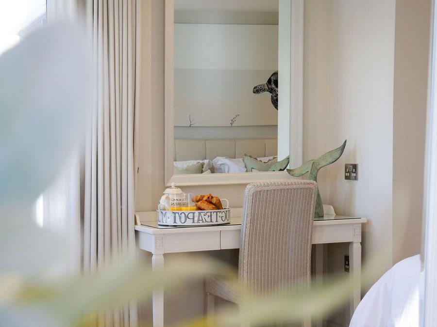 Vanity table with mirror, food tray, and whale tail sculpture in a cream-colored room.