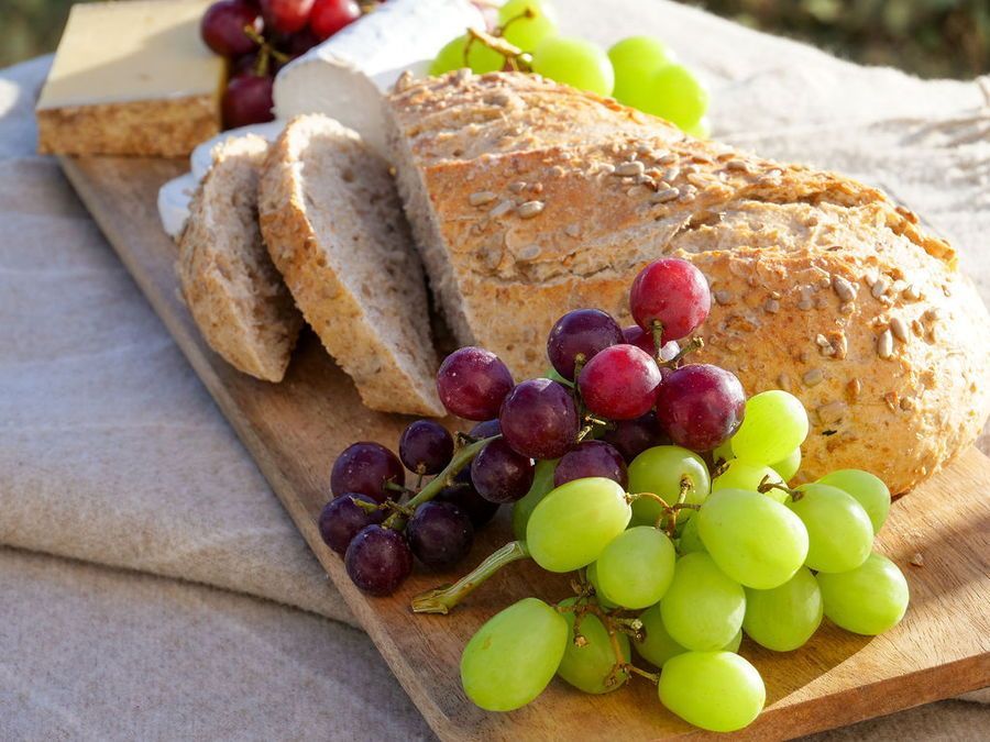 Wooden board with sliced bread, cheese, and green and purple grapes.
