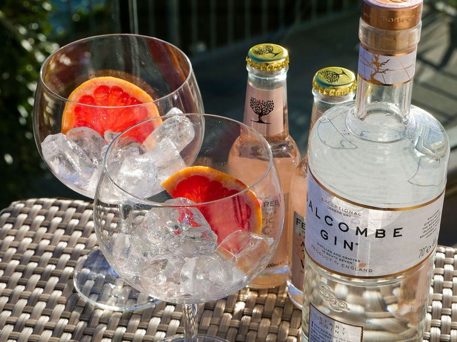 Gin and tonic with grapefruit slices, ice, and bottles on a wicker table.