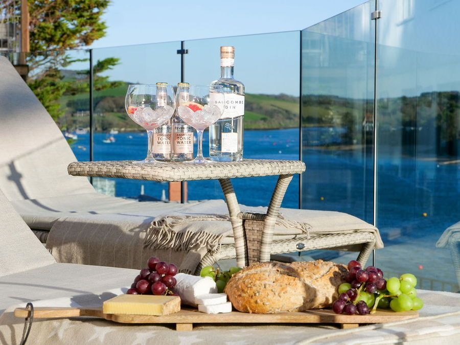 Table with food and drinks on a sun lounger overlooking a blue water view.
