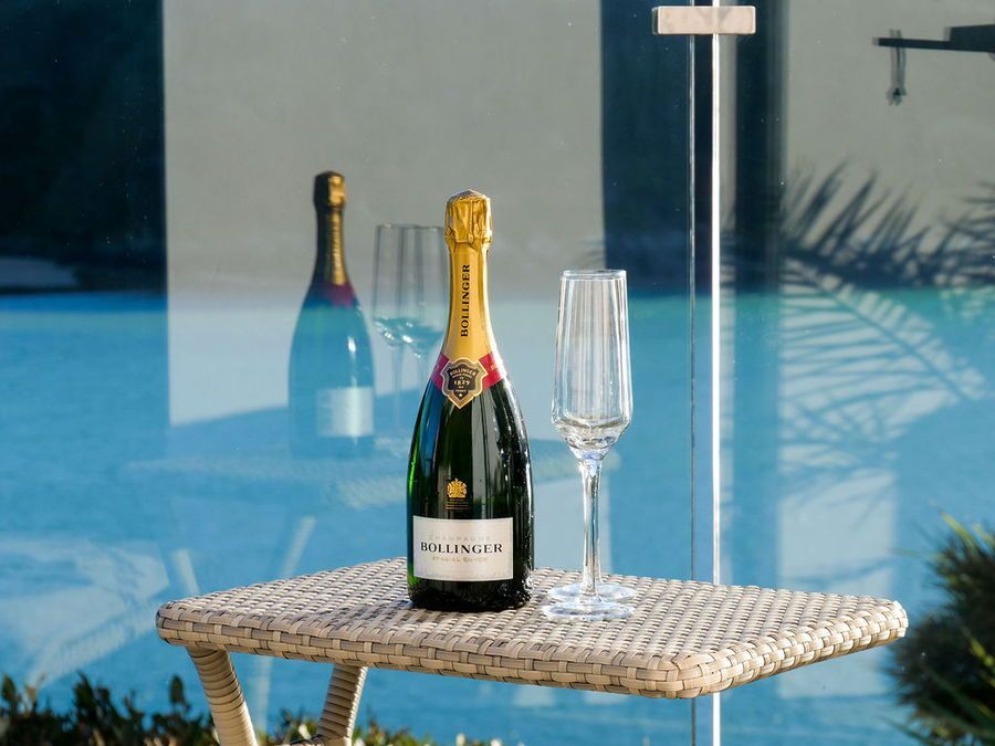Bottle of champagne and glass on a table by a pool, reflected in glass.