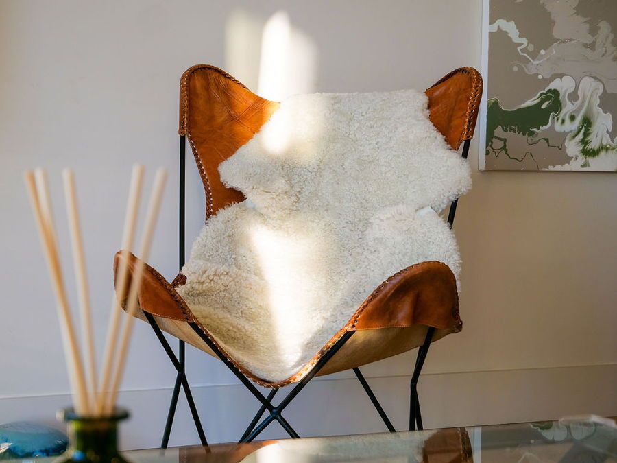 Leather butterfly chair with a white sheepskin throw, next to a wall with artwork.