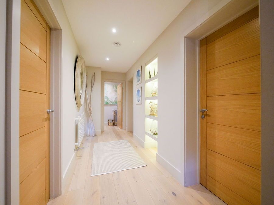 Hallway with light wood floors and doors, recessed shelving with artwork, and a rug.