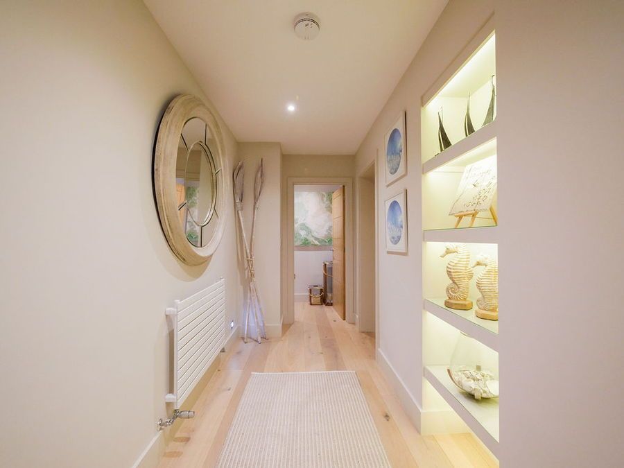 Long hallway with light wood floor, recessed shelving with illuminated art, round mirror, and radiator.