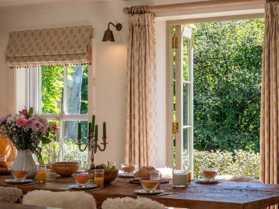Dining table set for a meal near an open window overlooking greenery.