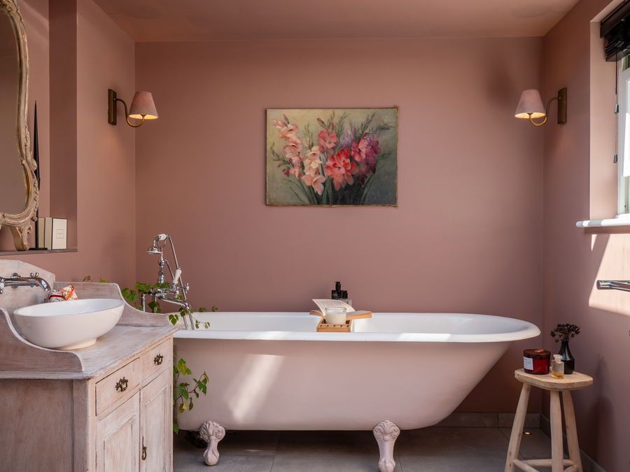 Pink-walled bathroom with a clawfoot tub, wood vanity, and floral painting.