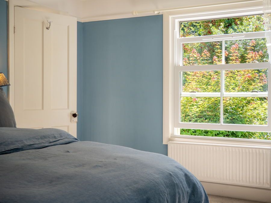 Bedroom with a blue wall, white window and door, and a bed with blue linens.