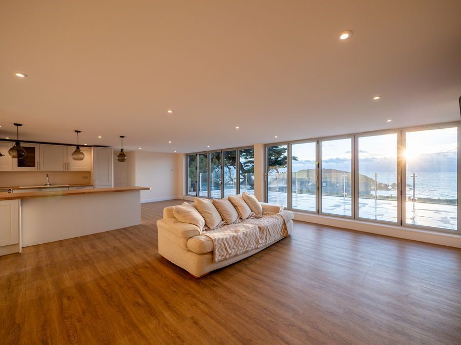 Bright living space with sofa, wooden floors, and expansive windows overlooking a coastal view.