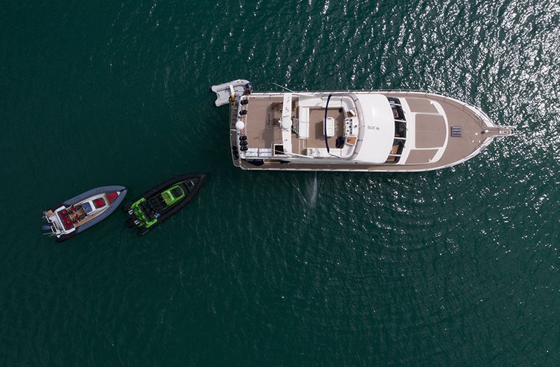 Overhead view of a yacht with two small boats in turquoise water.