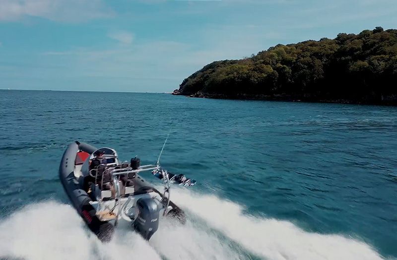 A black speedboat races across blue water near a forested island under a sunny sky.