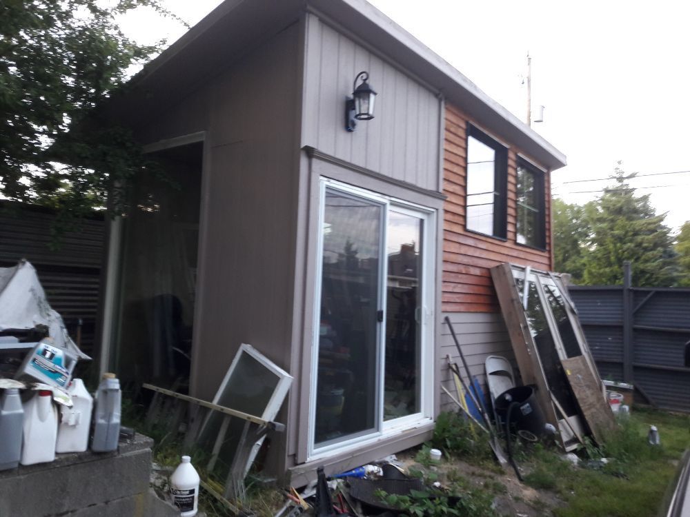 A shed with a sliding glass door is surrounded by junk
