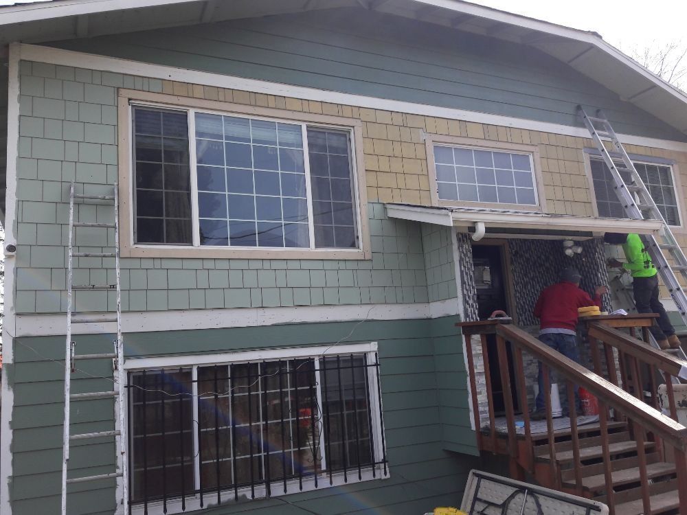 A man is painting the side of a house with a ladder.
