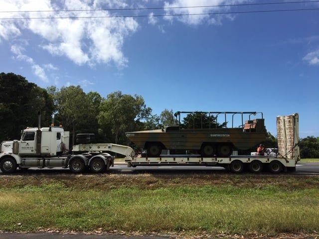 A Semi Truck is Carrying a Military Vehicle on a Trailer — Kelly's Crane Hire in Mossman, QLD