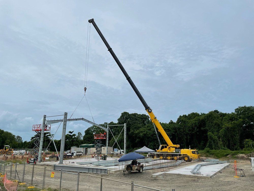 A Large Yellow Crane is Lifting a Metal Structure on a Construction Site — Kelly's Crane Hire in Mossman, QLD