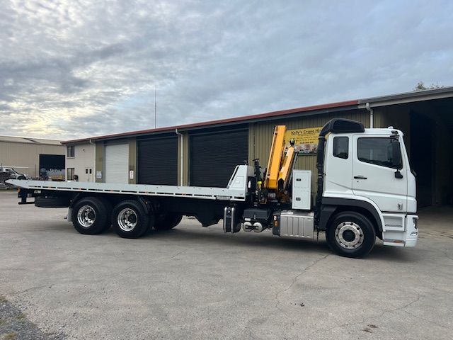 A White Dump Truck is Parked in a Grassy Field Next to a Boat — Kelly's Crane Hire in Mossman, QLD