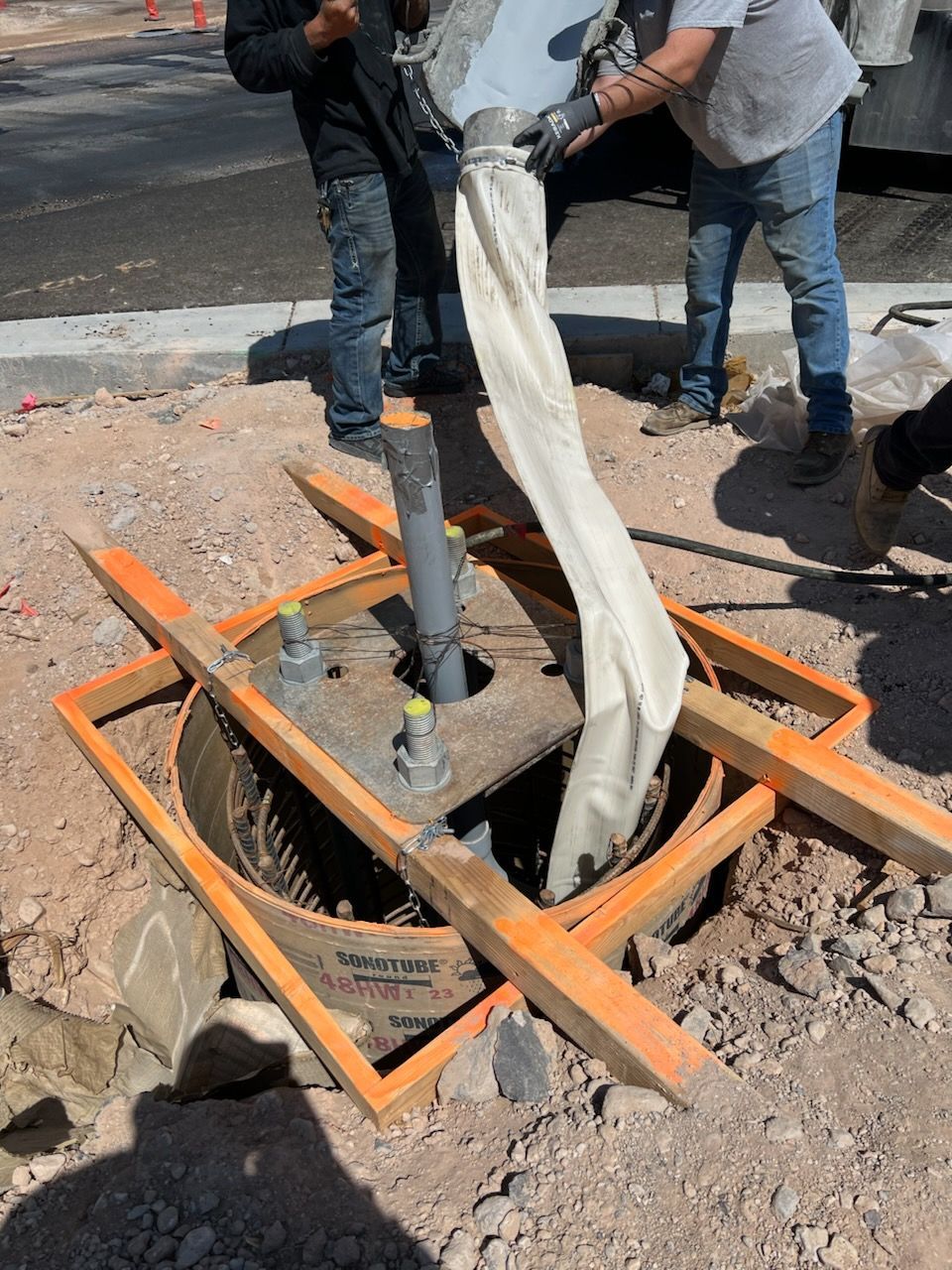 Concrete being poured into a circular form in a construction site; two workers involved.