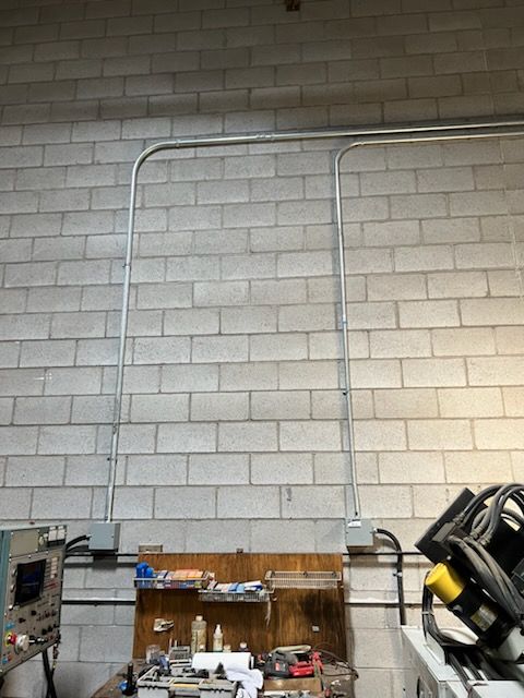 Conduit running vertically and horizontally on a brick wall. Electrical boxes near a workbench.