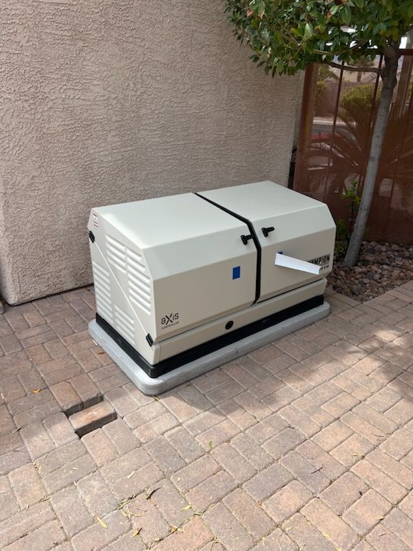Generator on a brick patio next to a stucco wall, beige and black casing.