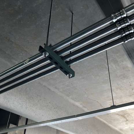Four parallel metal pipes suspended from a concrete ceiling, held by metal supports.
