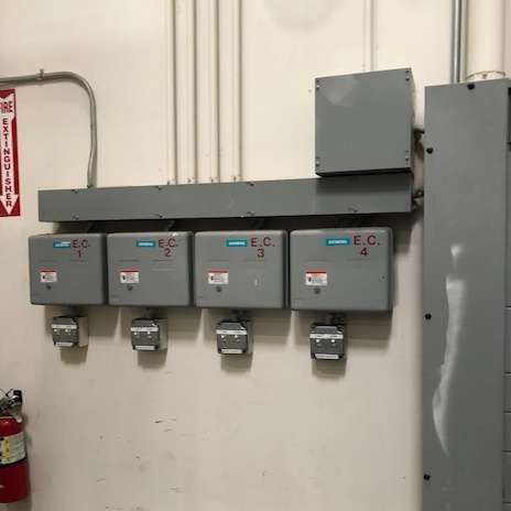 Electrical control boxes labeled E.C. 1-4 on a wall with conduit and a fire extinguisher.