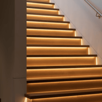 Wooden staircase with warm under-step lighting, ascending against a white wall.