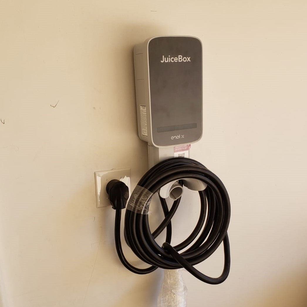 EV charger on a wall with a cord wrapped around a holder; black, gray, and white.