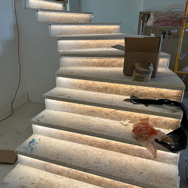Staircase with built-in lights, concrete steps. A box, debris, and plastic bag are on the steps, indoors.