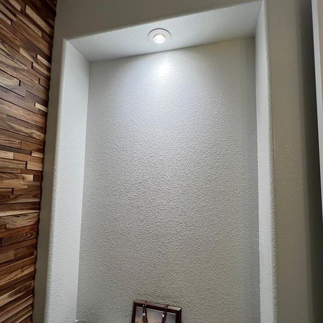 Recessed wall niche with speckled gray texture, lit by a centered overhead light, next to a wooden wall.