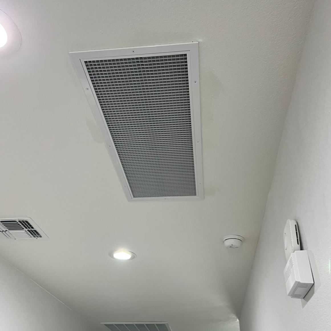 Ceiling with a long rectangular light fixture, air vents, and a smoke detector.
