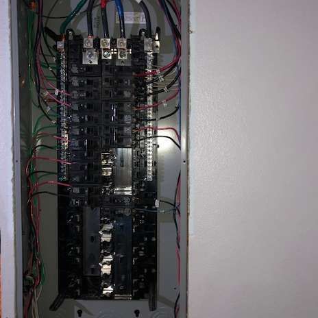 Electrical panel with wires and circuit breakers inside a metal enclosure.