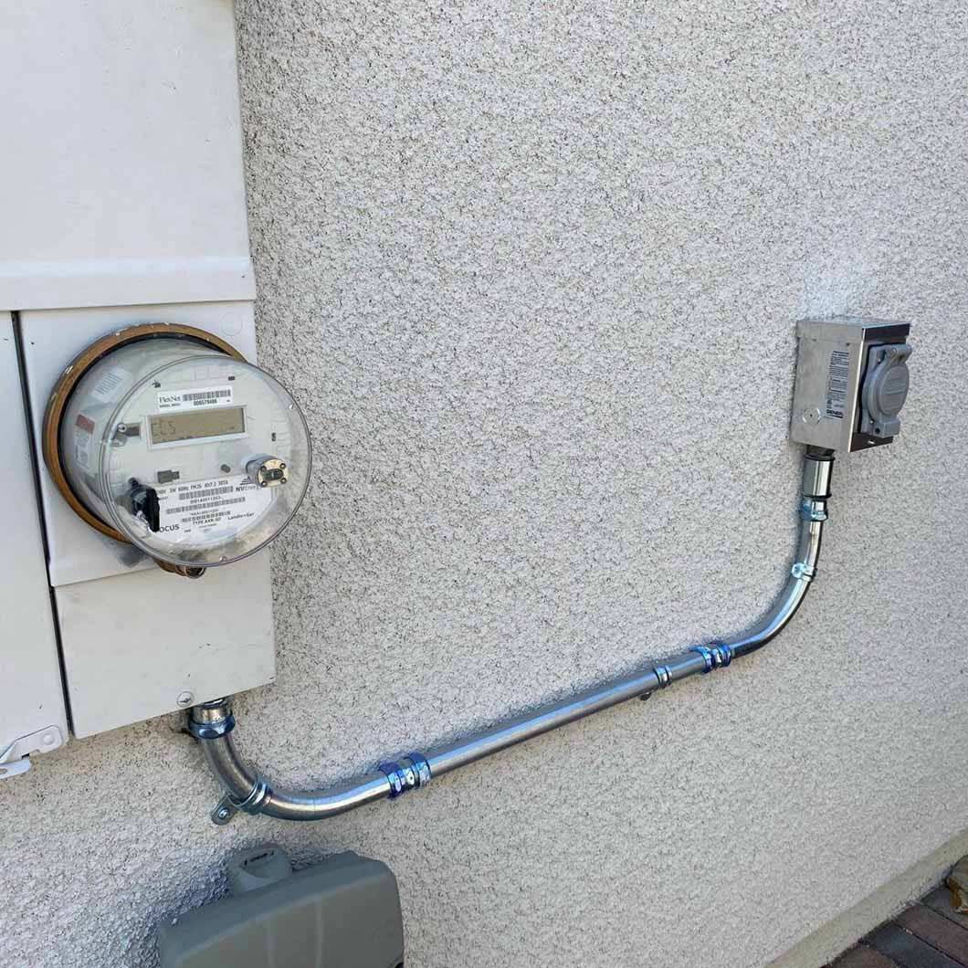 Electric meter and outlet box connected by conduit on a stucco wall.