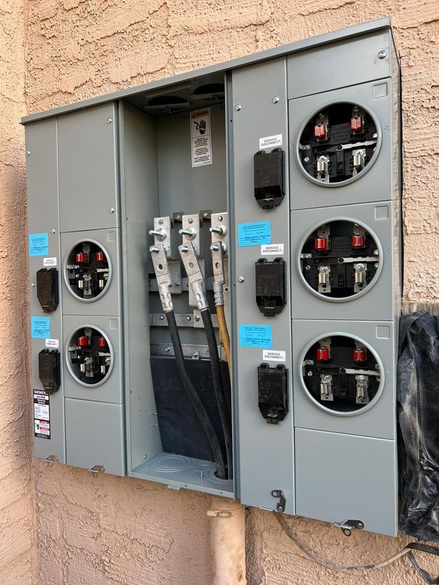 Gray electrical meter box with multiple meter sockets on a beige stucco wall.
