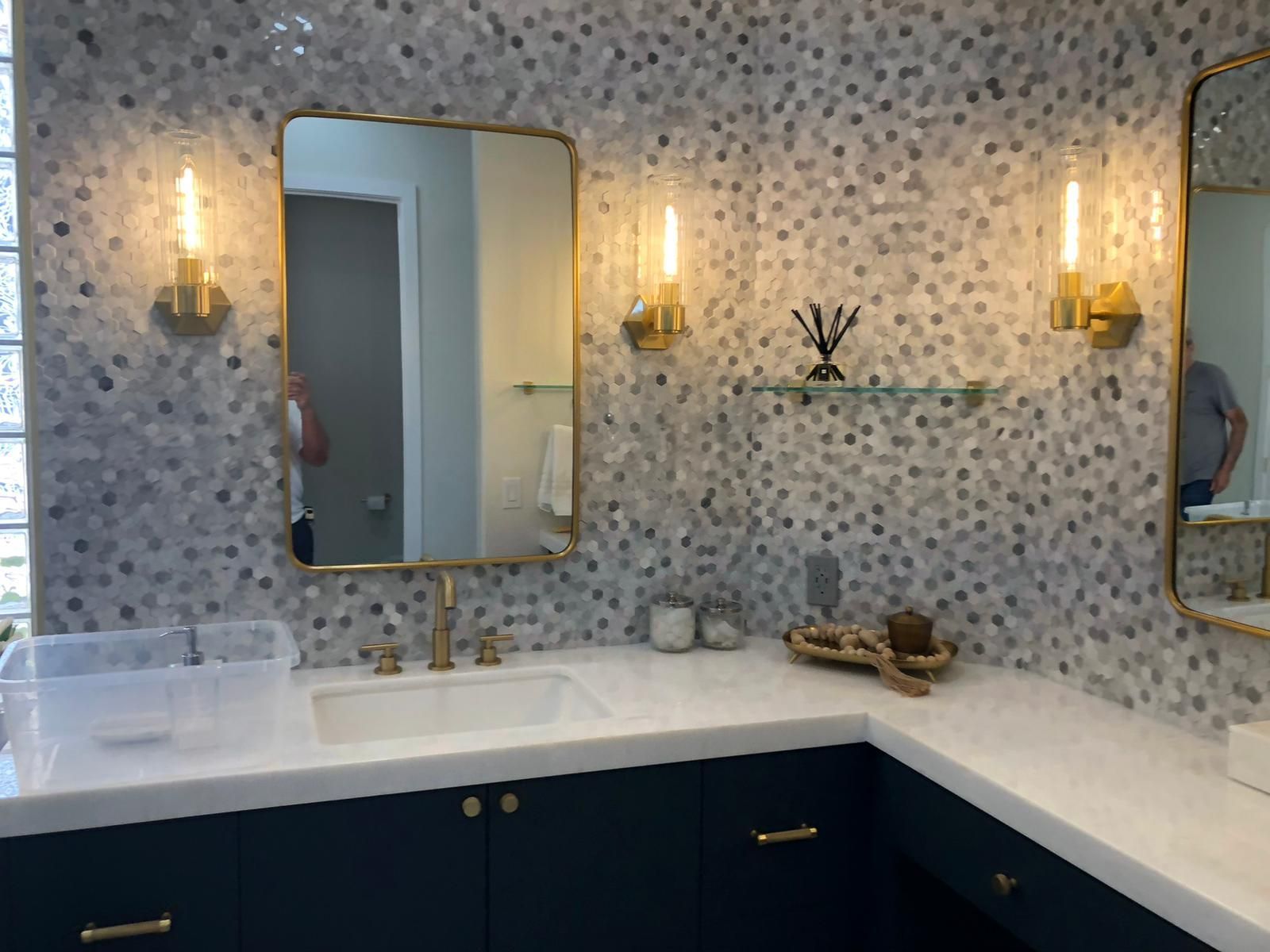 Bathroom with mosaic tile wall, gold fixtures, navy vanity, and a rectangular mirror.