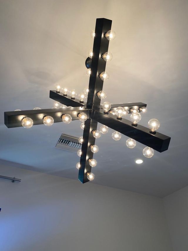 Black chandelier with many round, glowing light bulbs hangs from a white ceiling.