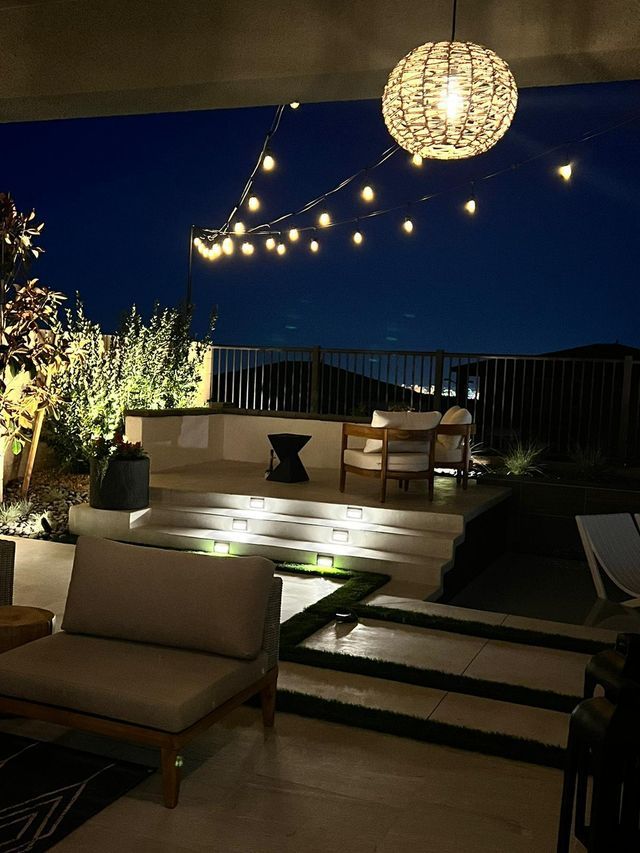 Outdoor patio at night, string lights, lit rattan globe, seating area with chairs, steps with greenery.