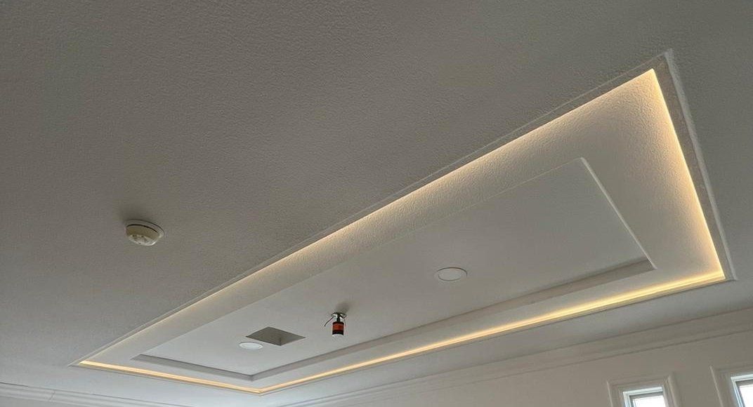 White ceiling with recessed rectangular lighting fixture and perimeter LED strip lighting.