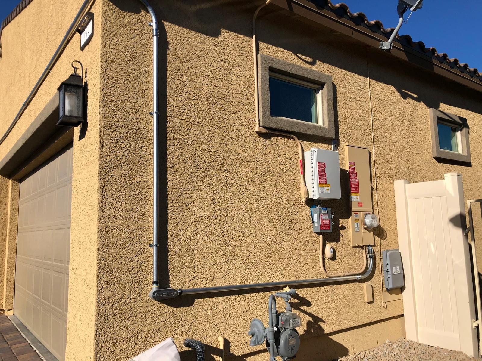Exterior of a stucco building with electrical equipment and conduit on the wall. A garage door and windows are also visible.